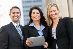 Businessman And Businesswomen Using Digital Tablet Outside Looking At Camera Smiling In Street